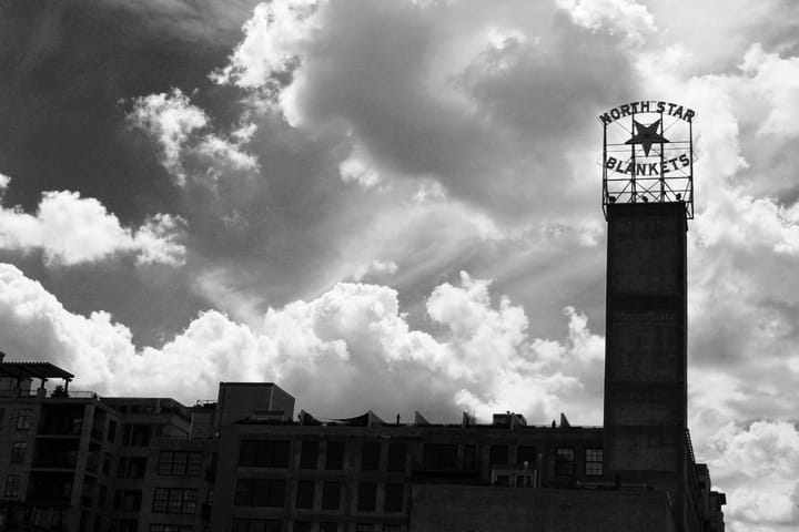A black and white image of an old warehouse, the sign reads, "North Star Blankets". Clouds gather in the background.